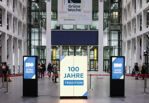Eingangshalle der Internationalen Gr&uuml;nen Woche in Berlin mit Banner &bdquo;Gr&uuml;ne Woche&ldquo; und Display &bdquo;100 Jahre Tradition&ldquo;.