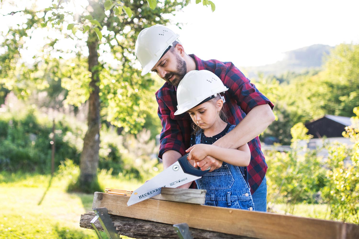 Das Titelbild zur Erfolgsstory der MBG Berlin-Brandenburg zeigt einen Mann und ein Kind die gemeinsam mit einer Säge von Augusta Heckenrose Werkzeugfabriken eine Holzlatte sägen