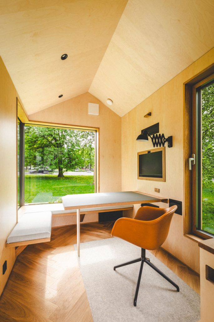 Ausgestatteter Innenraum eines mobilen Meetingraums von TINY SPACE mit Tisch, Sitzbank und Monitor – sofort einsatzbereit auf Events und Konferenzen.