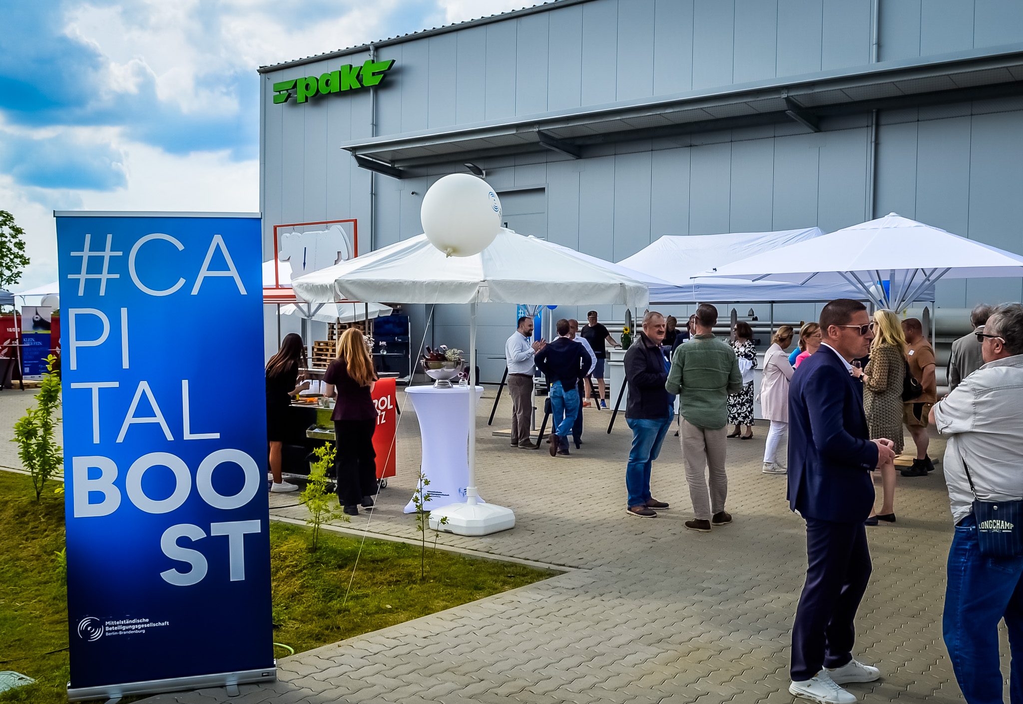 Networking beim Capital Boost 2026: Gäste vor dem Unternehmensstandort, MBG-Rollup „Capital Boost“ und Gespräche im Außenbereich unter Sonnenschirmen.